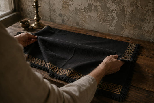 Des mains dépliant une nappe d’autel noire à franges et motifs celtiques sur une table de bois