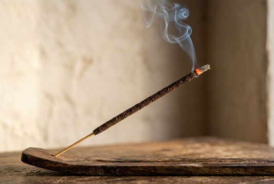 Un bâtonnet d'encens se consume sur un porte-encens en bois, devant un mur de plâtre