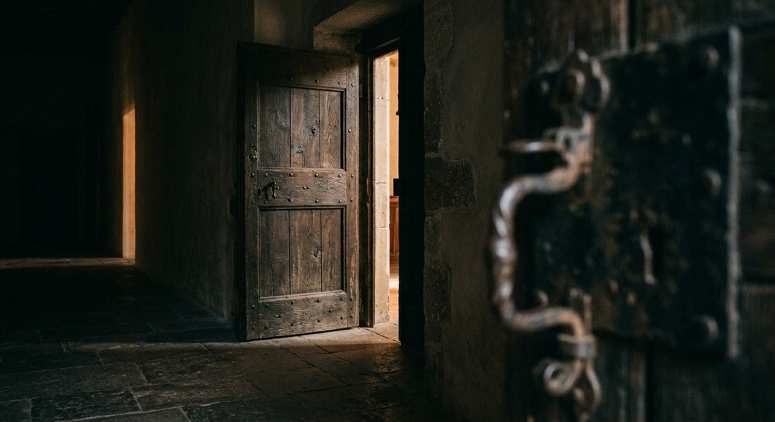 Une porte ancienne en bois entrouverte, lumière chaude filtrant dans un couloir de pierre sombre