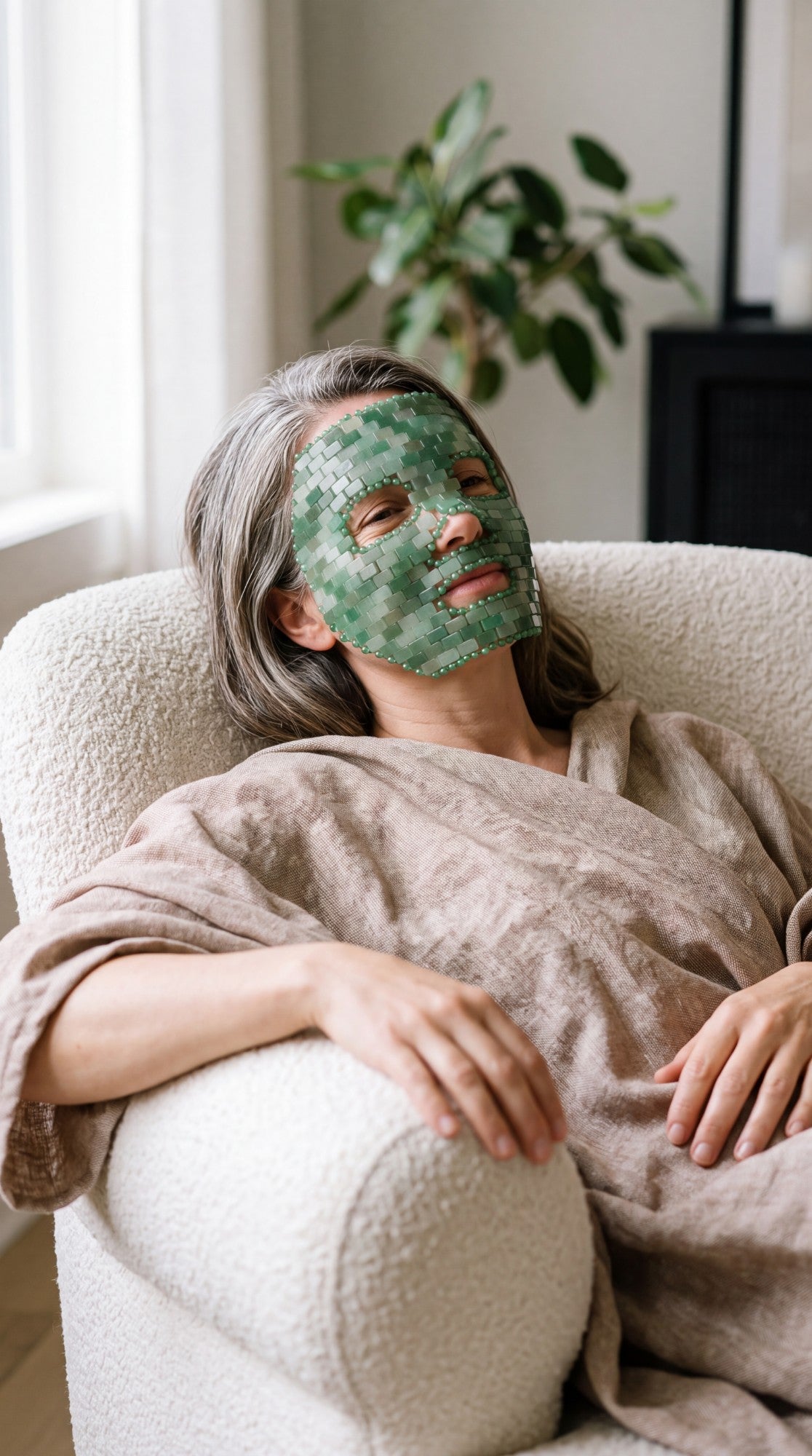 Femme d’environ 50 ans, détendue dans un fauteuil, portant un masque de visage en aventurine verte