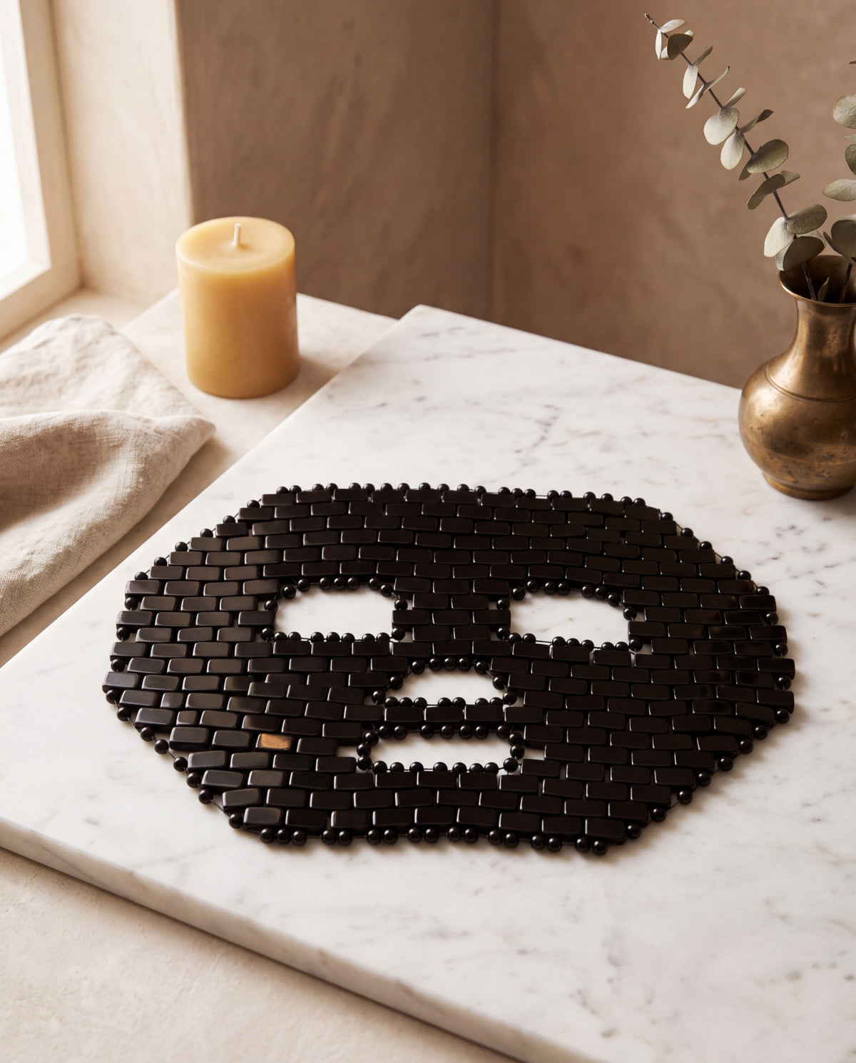 Masque de visage en mosaïque d’obsidienne, posé sur un présentoir en marbre blanc